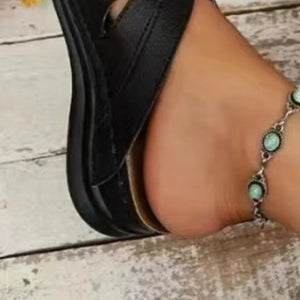 Black leather lace-up cutout slides with a decorative turquoise ankle bracelet.
