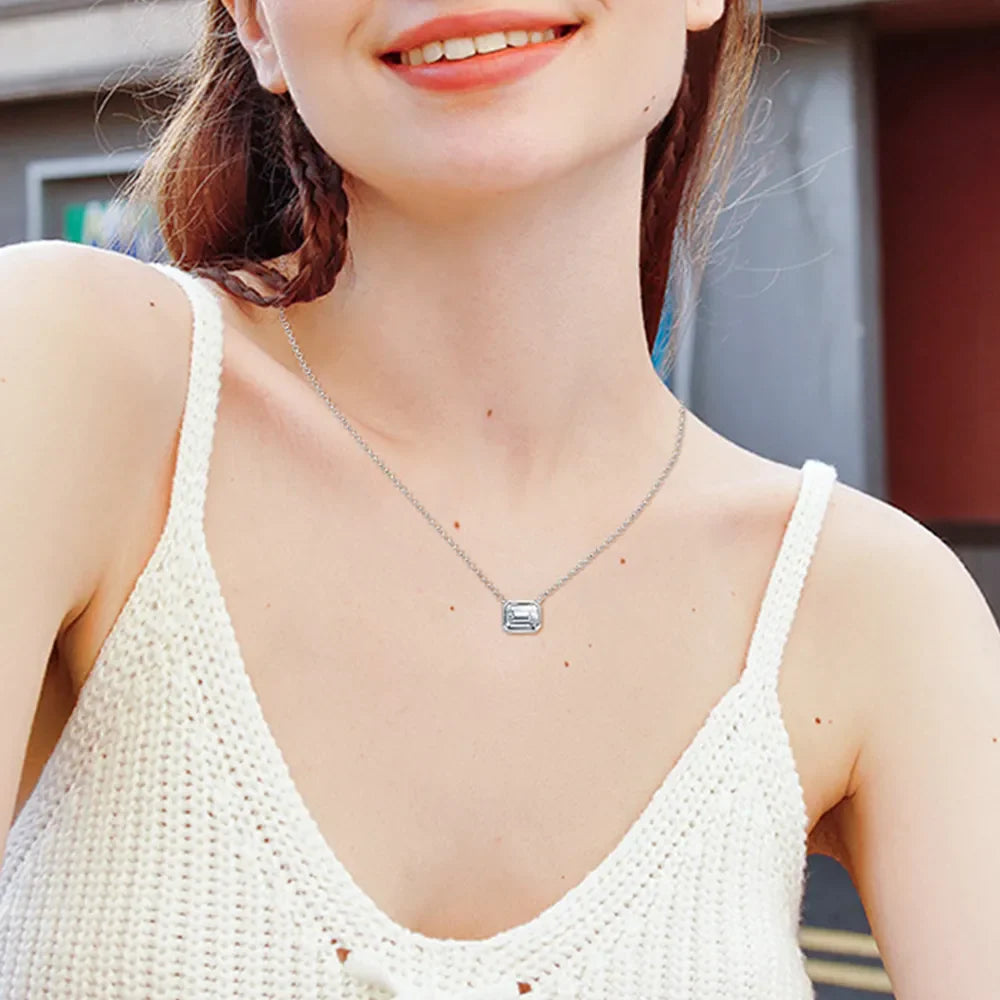 Silver necklace with emerald cut moissanite in a gold bezel setting.