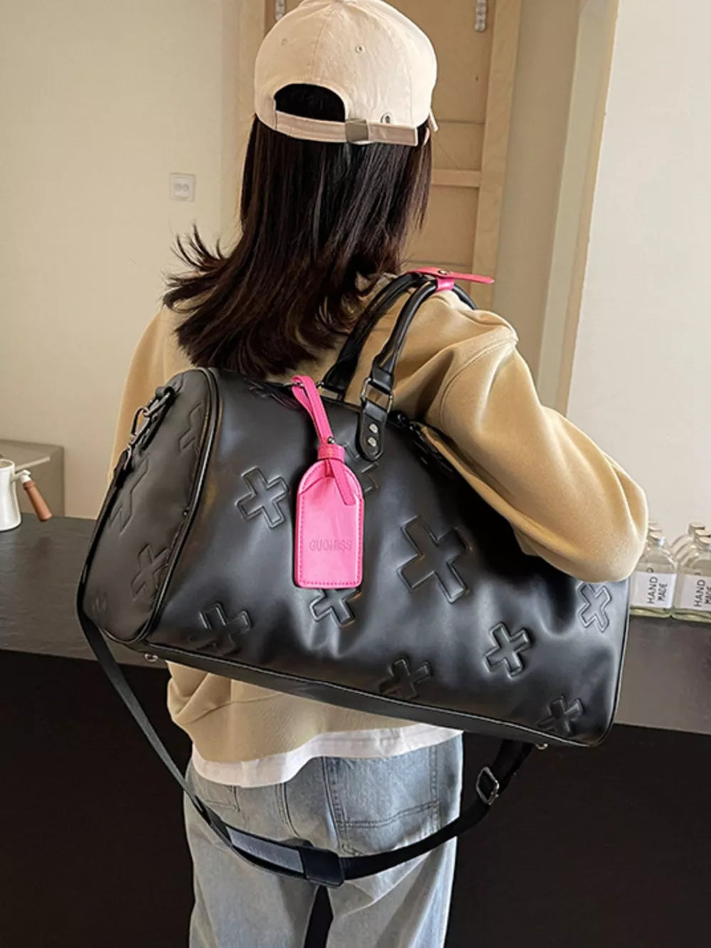 Black embossed cross detail luxury duffel bag with pink luggage tag