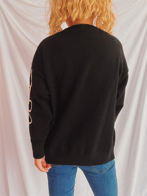 Black acrylic knit sweater with cream floral outline detail on sleeve