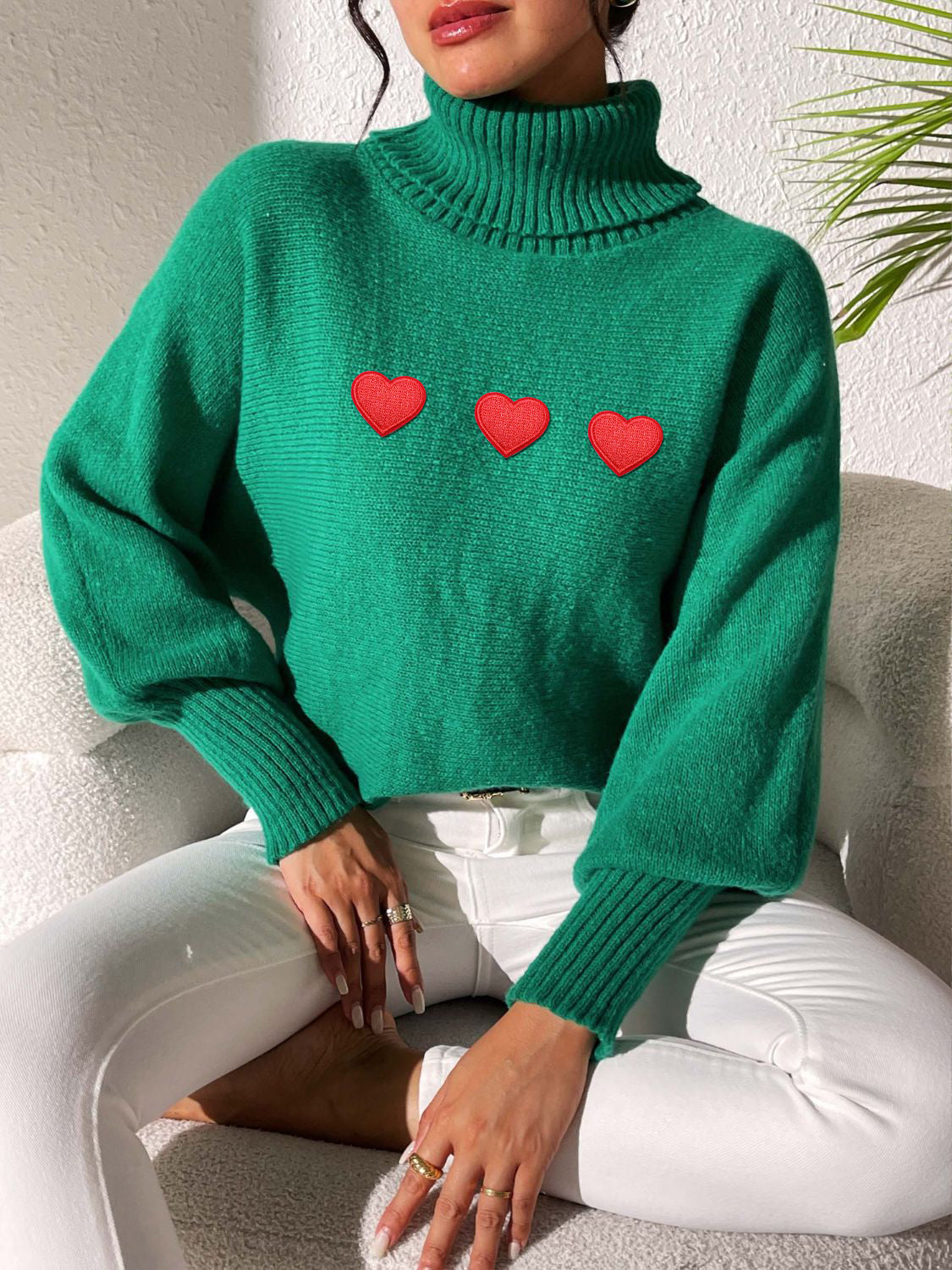 Green turtleneck sweater with balloon sleeves and red heart appliqués.