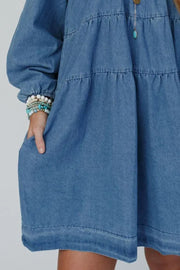 Tiered denim mini dress in medium wash with square neckline and pockets.