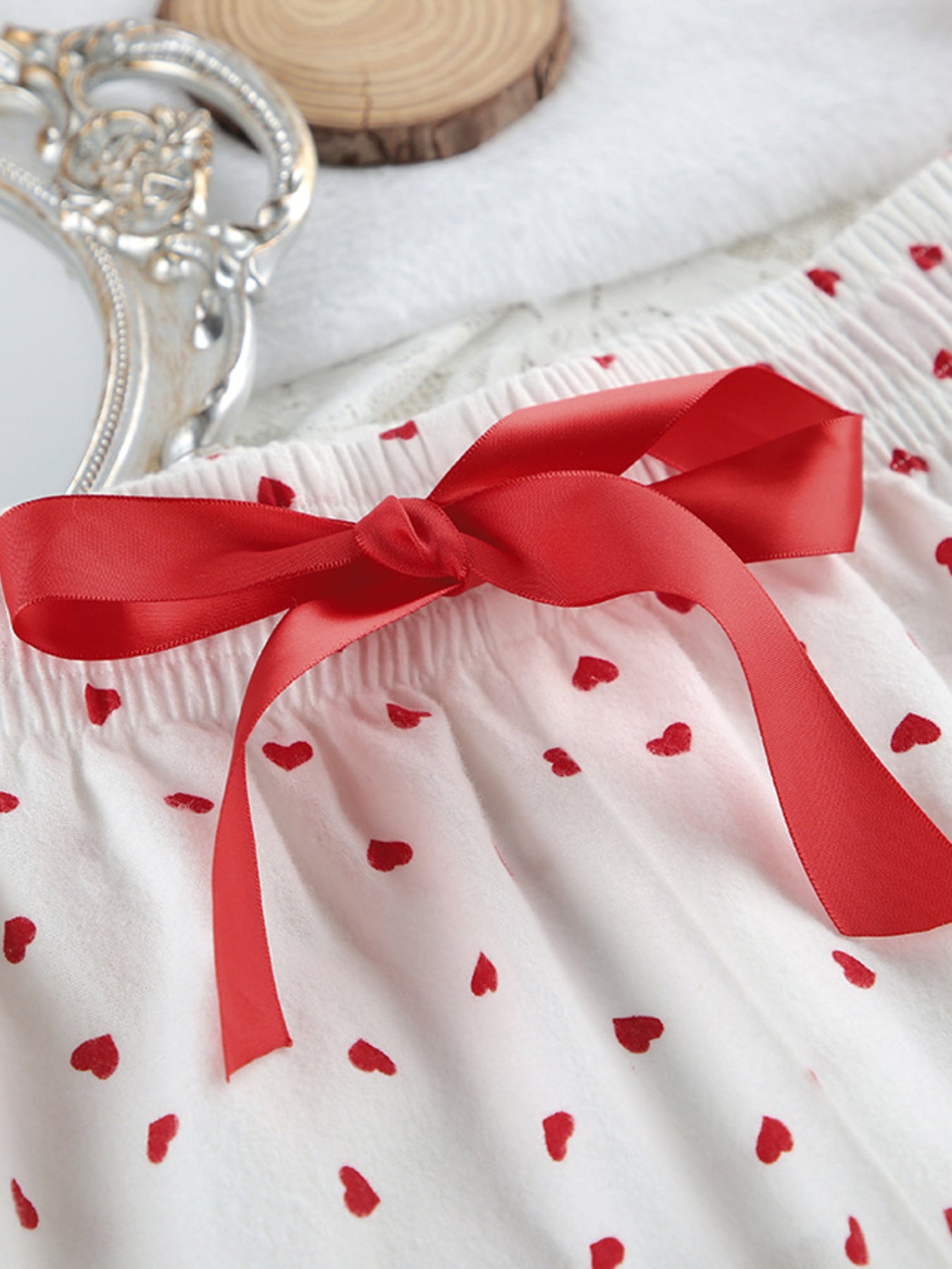 White cotton pajama shorts with red heart pattern and red satin bow detail.