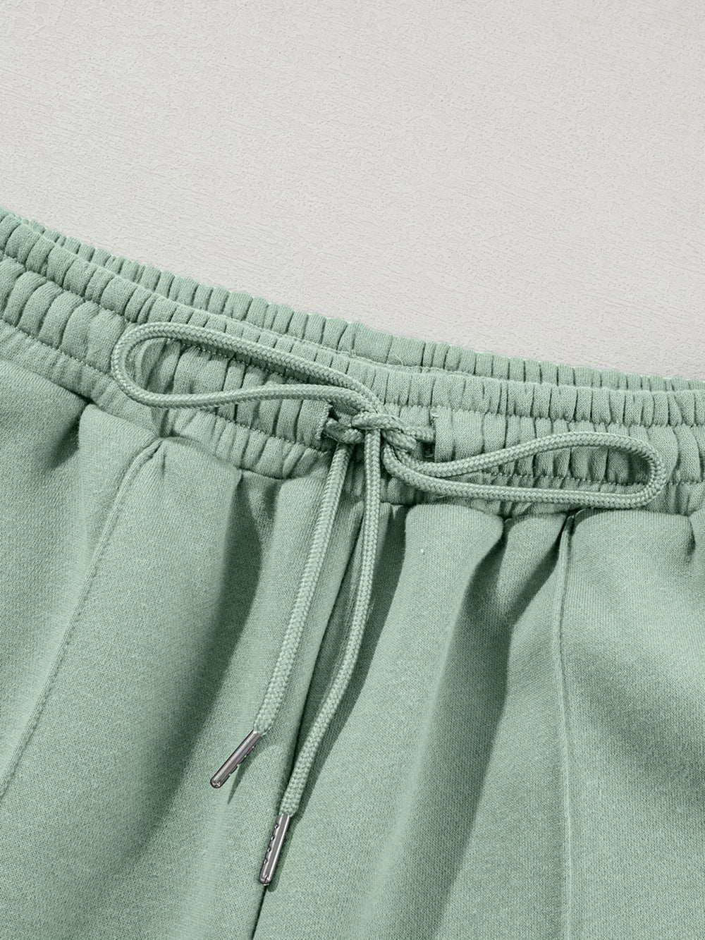 Sage cotton joggers with drawstring waist and silver-tipped ties.