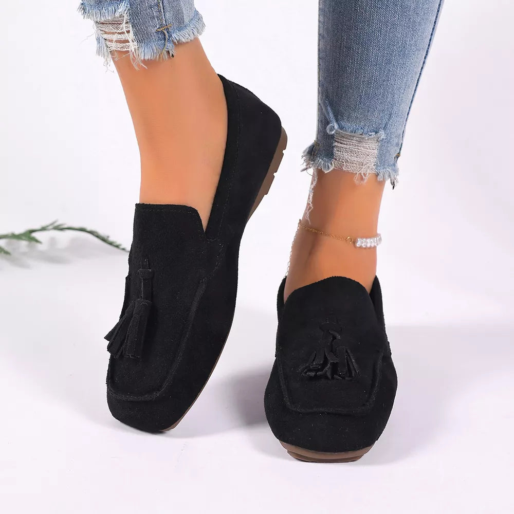 Black suede slip-on loafers with tassel detail.