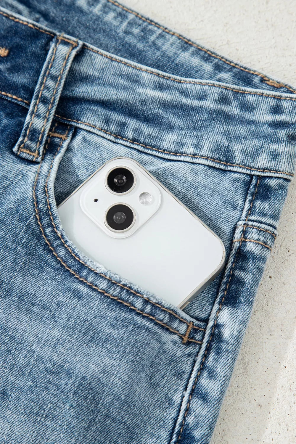 Distressed denim flare jeans with a white smartphone in the pocket