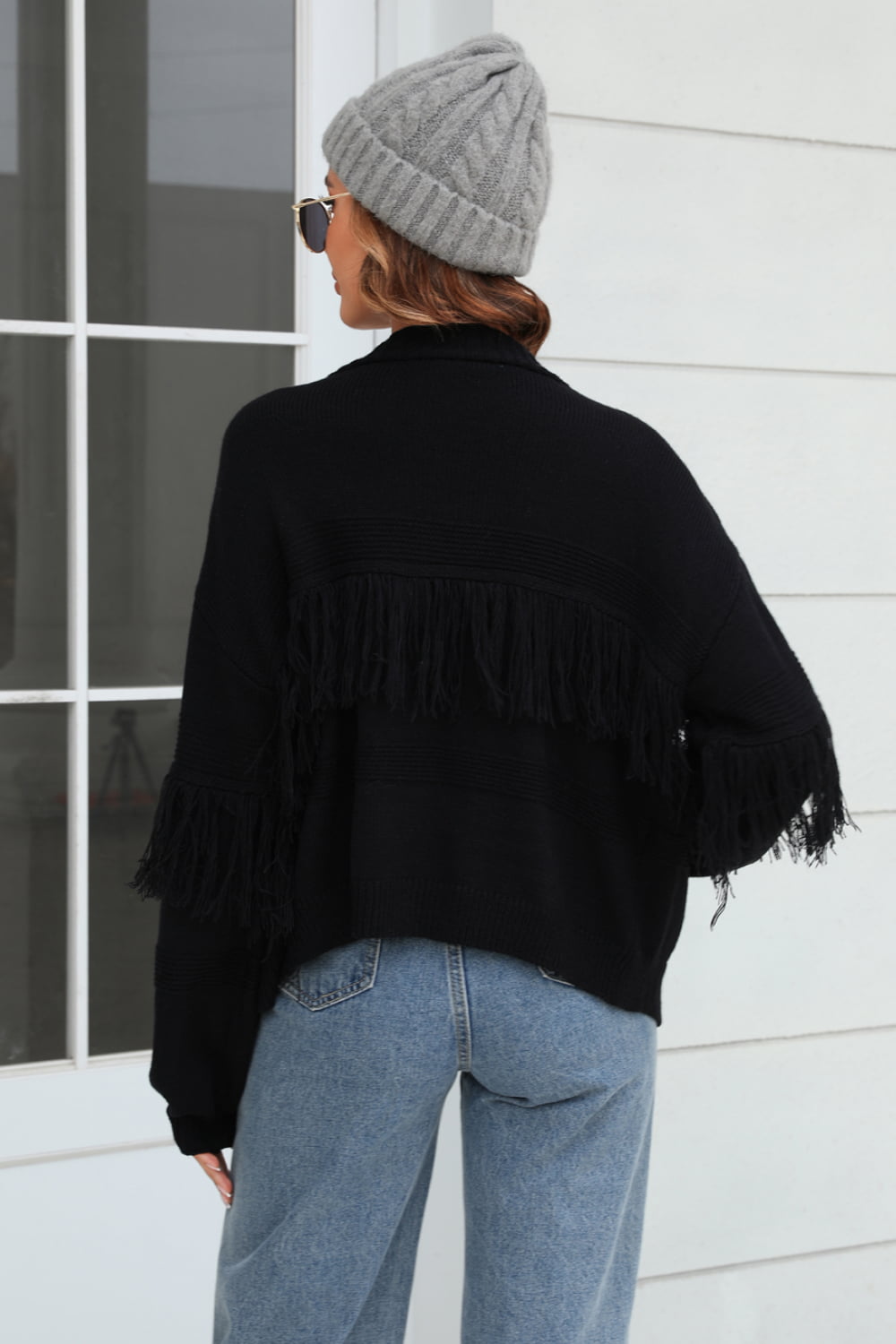 Black acrylic cardigan with fringe detail on sleeves and back, relaxed fit.