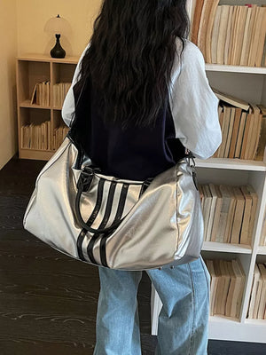 Sleek metallic silver duffle bag with black stripes and handles, worn by a woman.