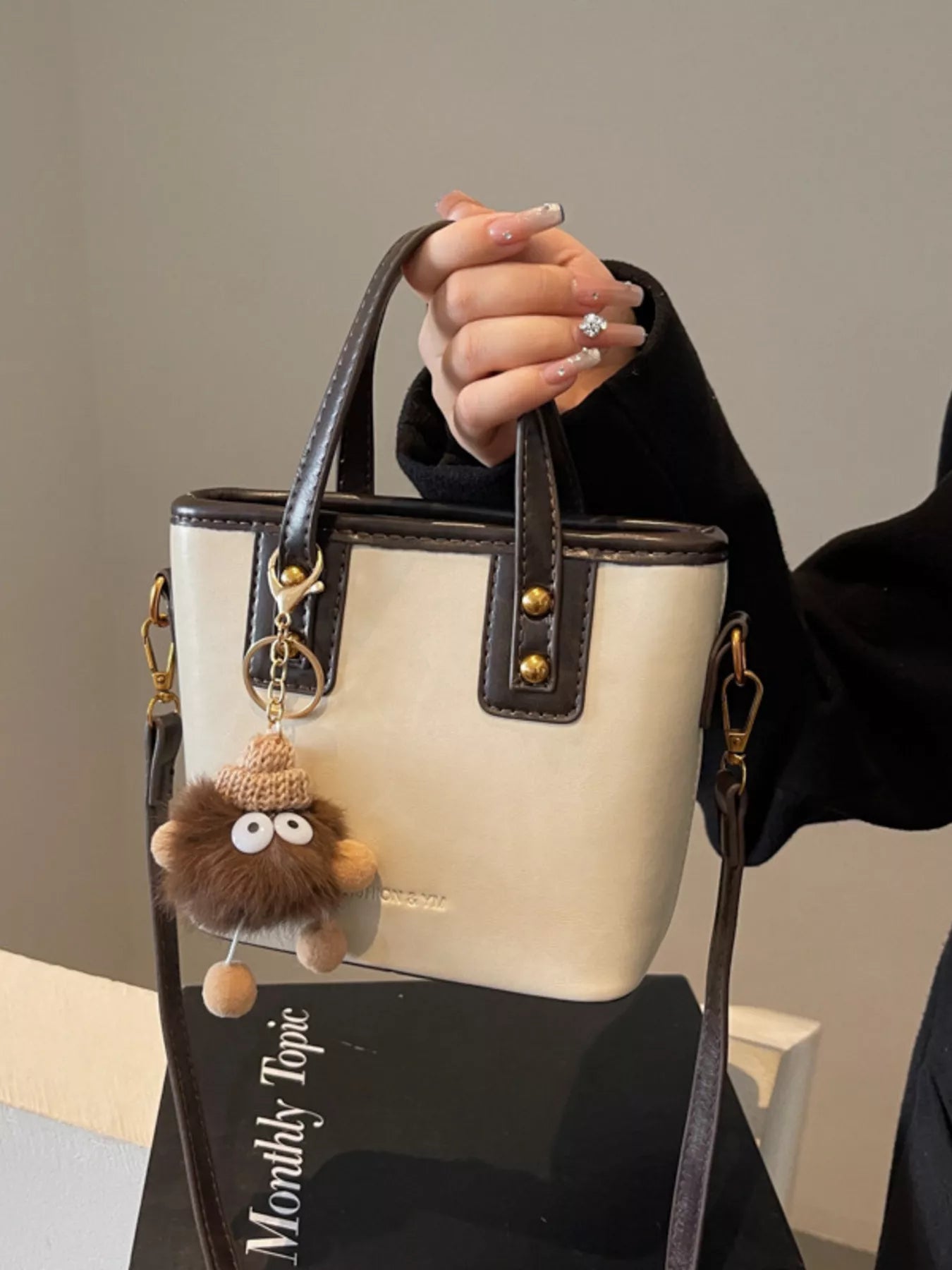 Mini leather crossbody bag in beige with brown trim and a fuzzy charm.