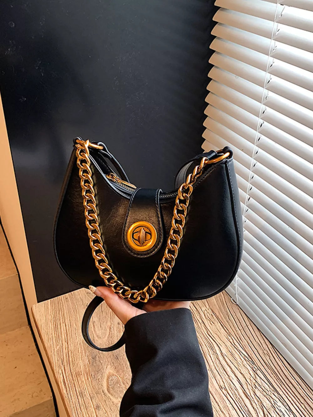 Black crescent mini shoulder bag with gold chain accent and turn-lock closure.