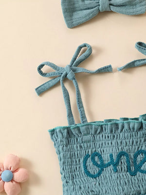Sea blue smocked baby bodysuit with tie straps and embroidered "one" detail, with matching headband.