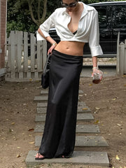 White cropped button-up shirt with open collar and long sleeves, styled with a black maxi skirt.