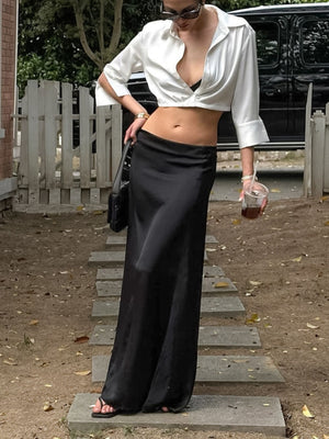 White cropped button-up shirt with open collar and long sleeves, styled with a black maxi skirt.