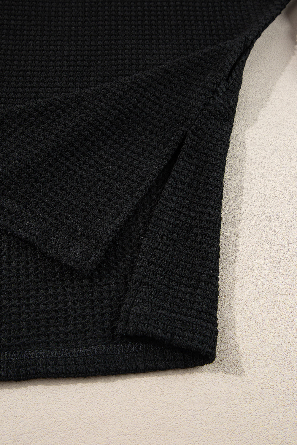 Black waffle knit sweater with V-neck and slit hem detail.