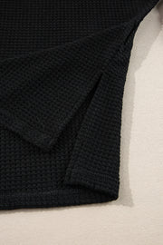 Black waffle knit sweater with V-neck and slit hem detail.