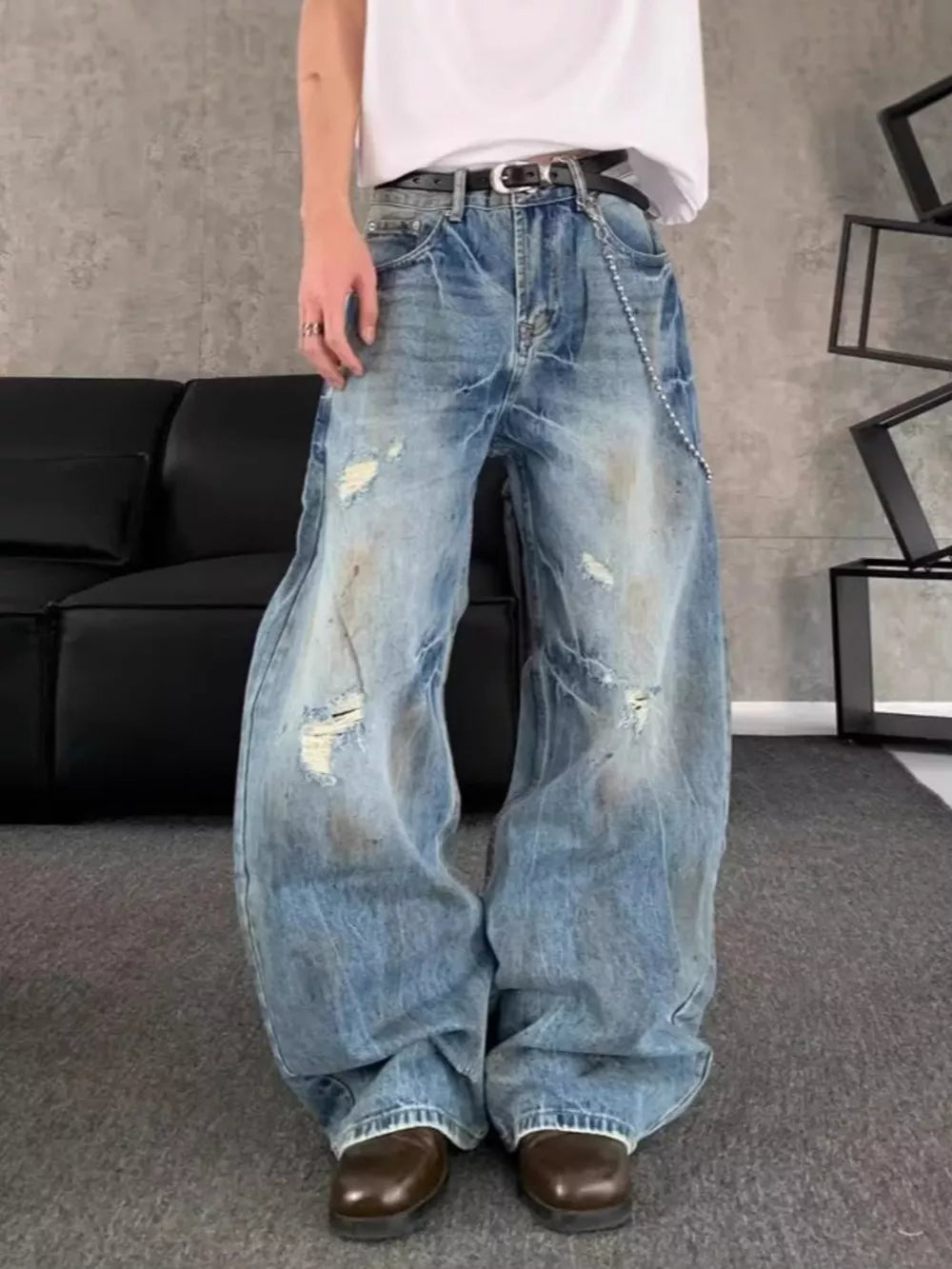 Distressed wide-leg denim jeans for men in light blue wash with chain detail.