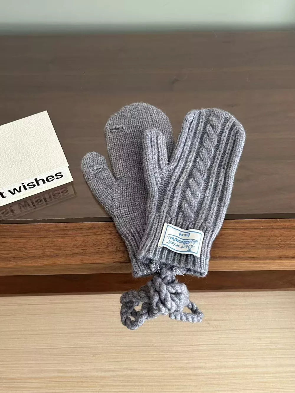 Gray cable knit acrylic gloves with braided detail and a knotted string.