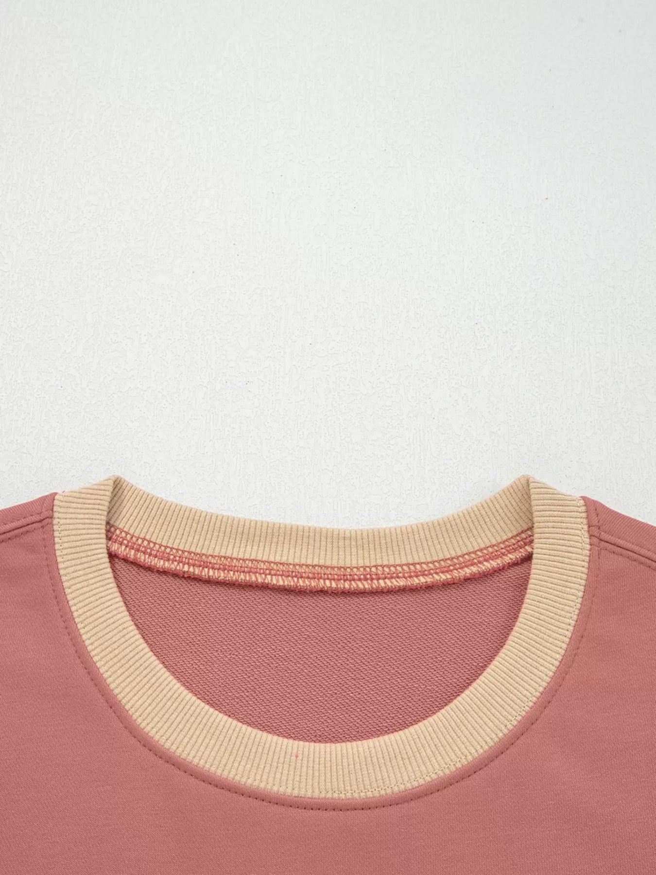 Dusty pink sweatshirt with contrast tan ribbed neckline and exposed seam detail.