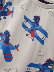 Toddler t-shirt with all-over print of blue cartoon airplanes with dinosaurs flying, on light grey fabric.