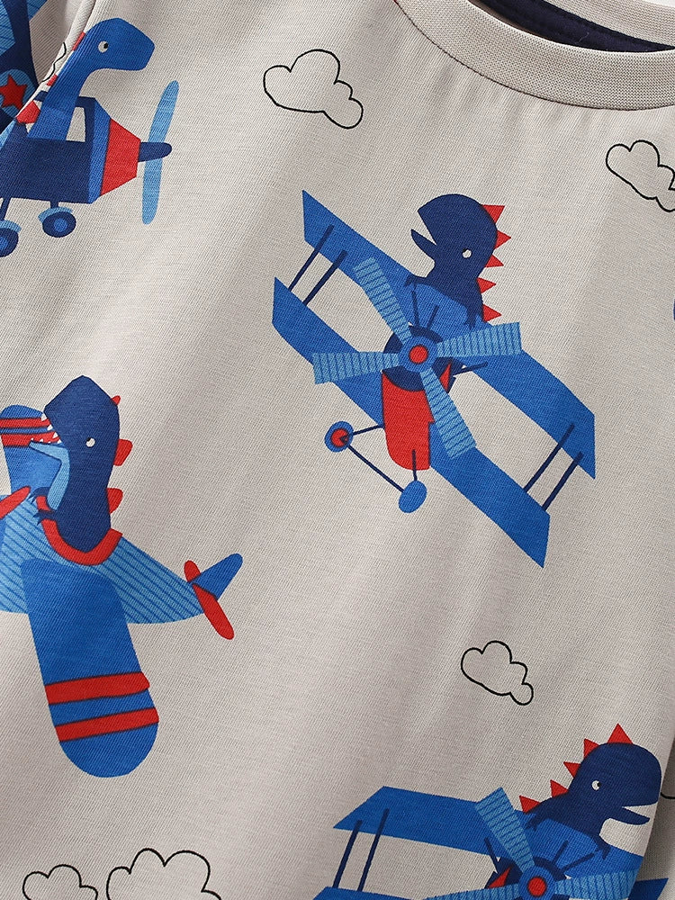 Toddler t-shirt with all-over print of blue cartoon airplanes with dinosaurs flying, on light grey fabric.
