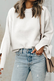 White textured knit sweater with crew neck and slit sleeves, styled with light wash jeans.