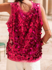 Hot pink sequin tank top with a sheer neckline and hem, styled with white pants.