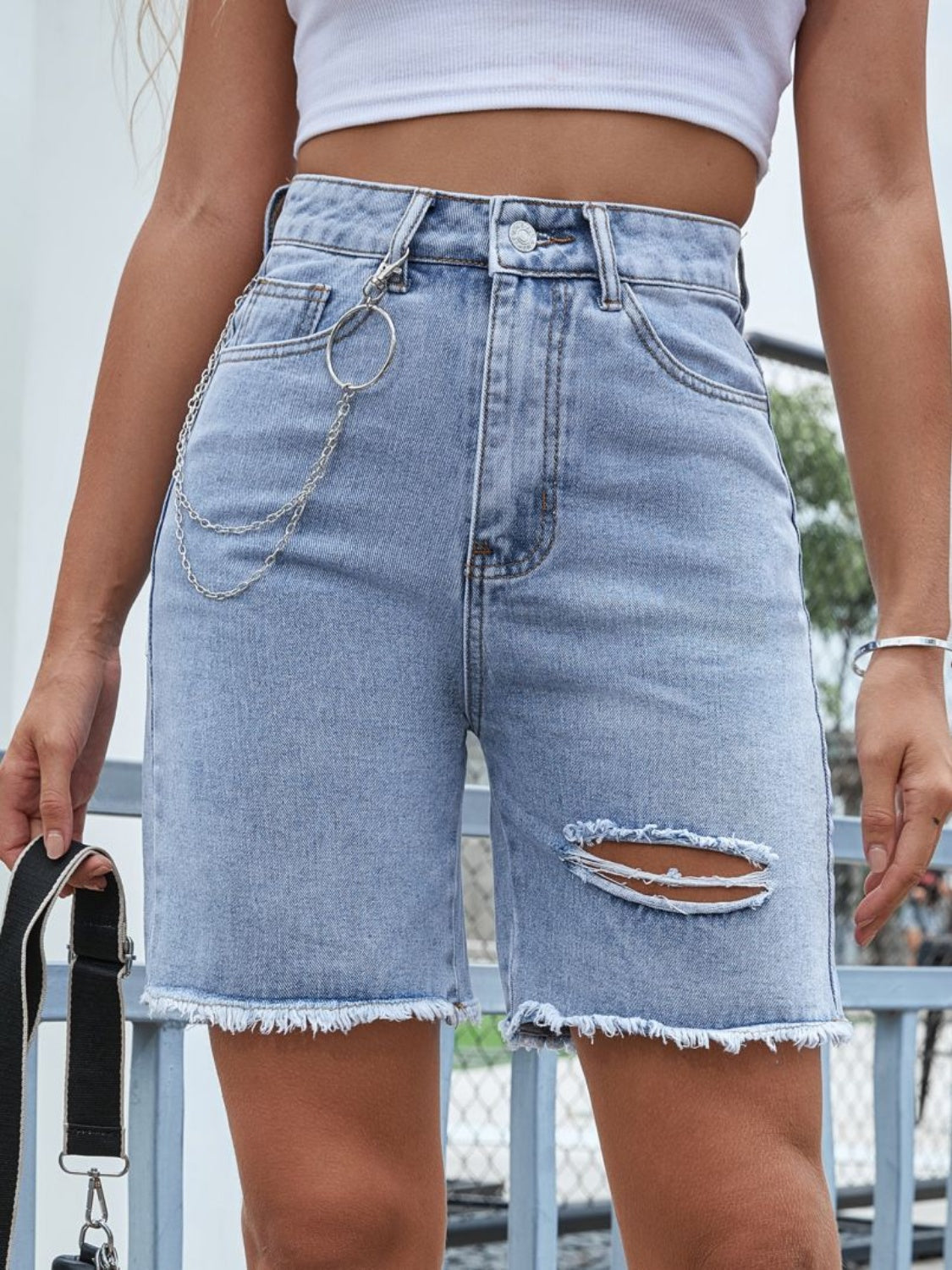 Light wash denim bermuda shorts with distressed details and a chain accessory.