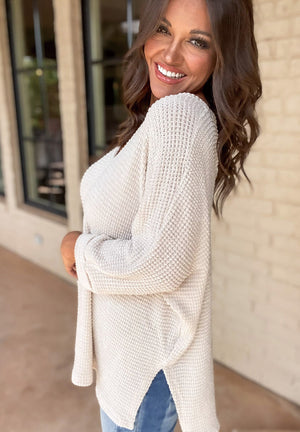 Beige waffle knit V-neck sweater with slit hem and long sleeves.