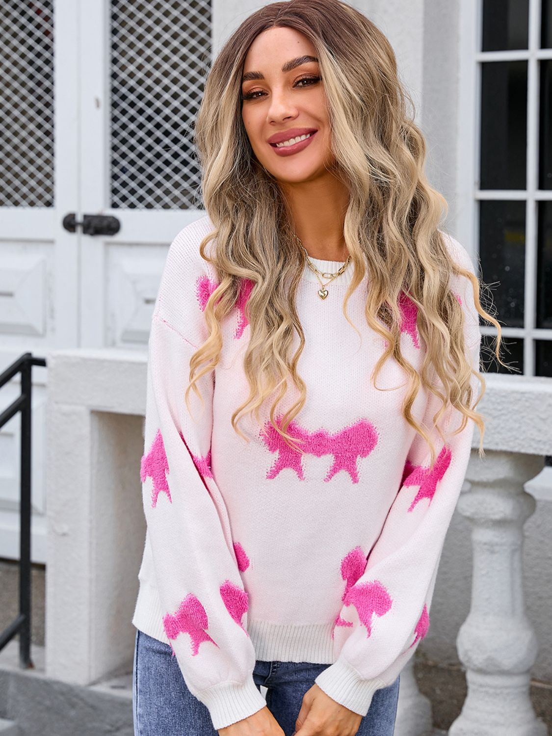 Pink knit pullover sweater with bow motif pattern and crew neck.