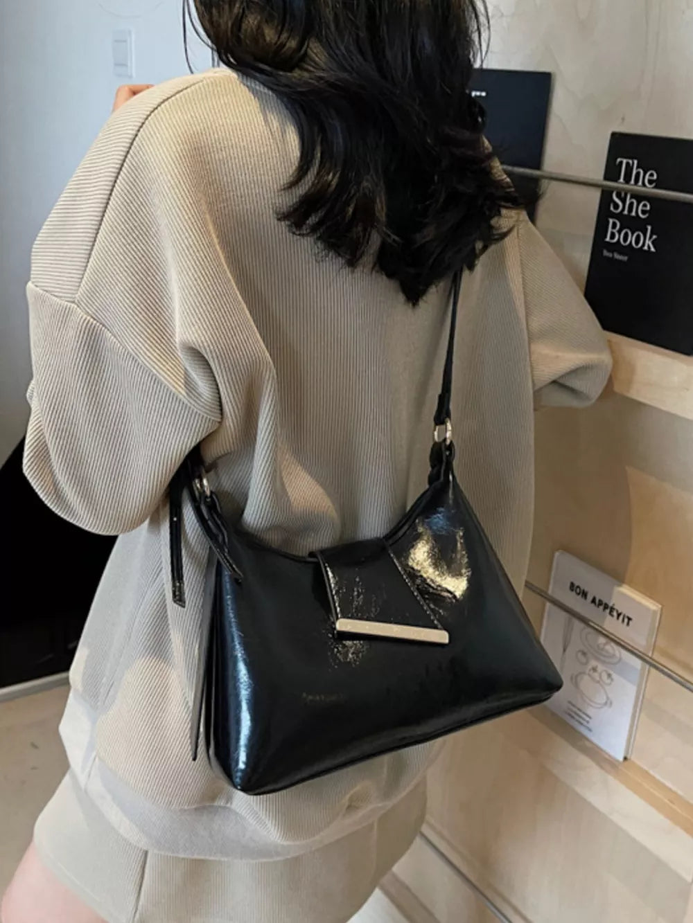 Black patent leather crossbody bag with gold hardware detail.