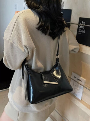 Black patent leather crossbody bag with gold hardware detail.