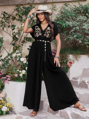 Black embroidered flutter sleeve wide-leg jumpsuit with a V-neck and gold chain belt.