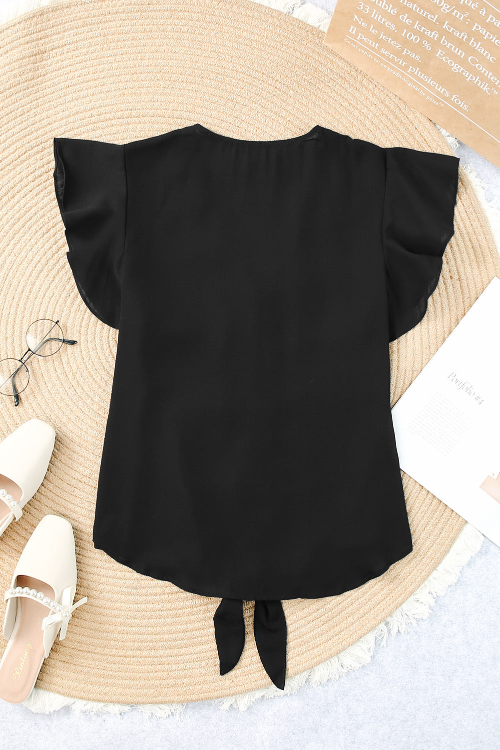 Black tie-front blouse with ruffle sleeves and a curved hem.