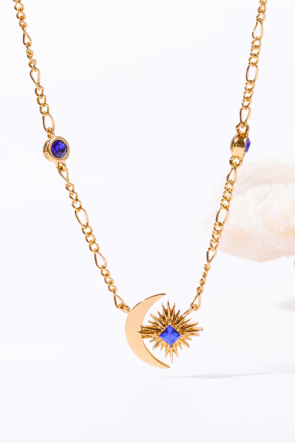 Gold celestial necklace with crescent moon, sunburst charm, and blue gems.