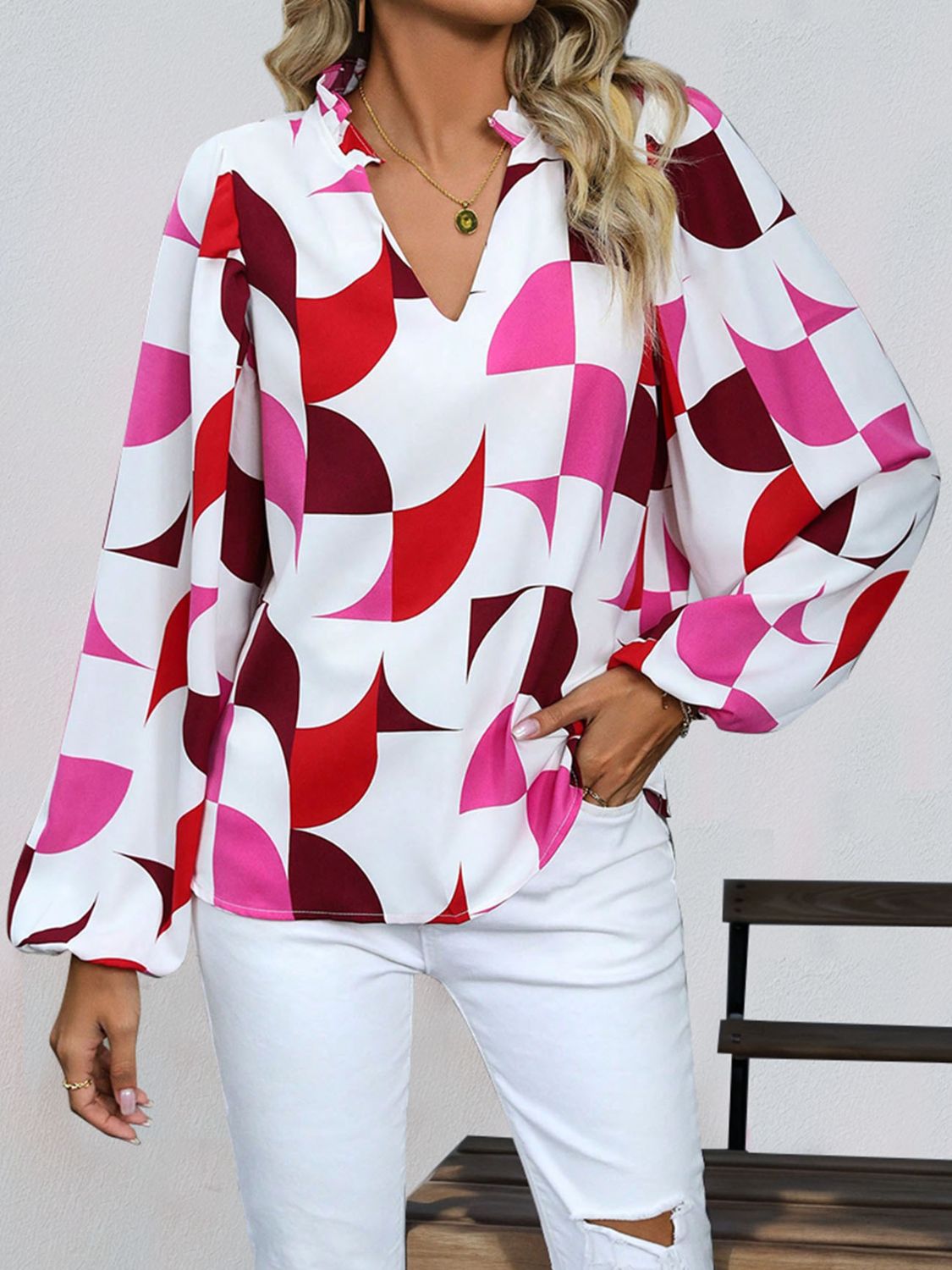Geometric print blouse with voluminous sleeves and a ruffled V-neck in white with red and pink shapes.