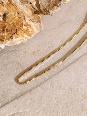 Gold layered necklace with a serpentine chain and cross pendant detail.