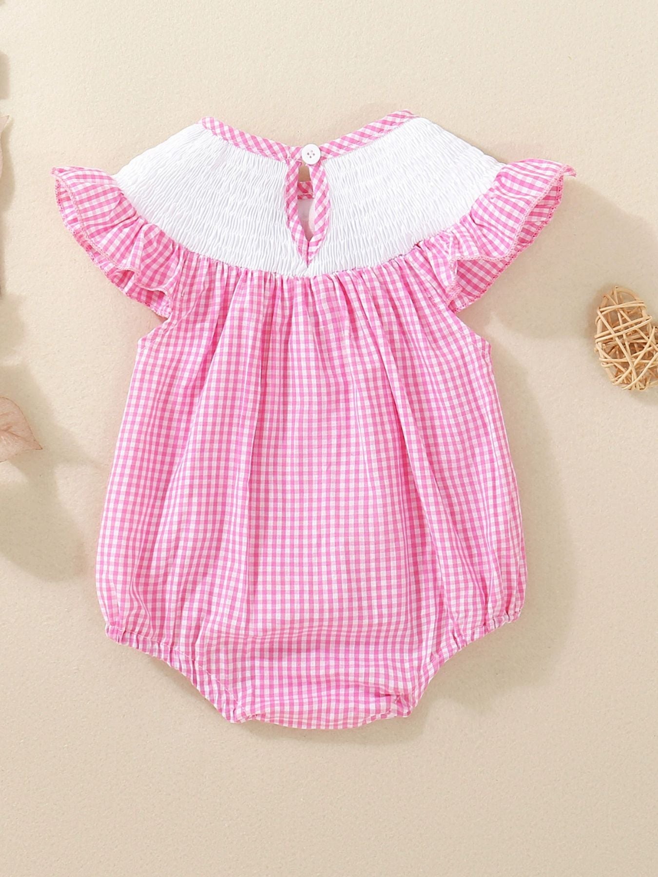 Pink gingham baby one-piece with smocked white bodice and ruffled sleeves.