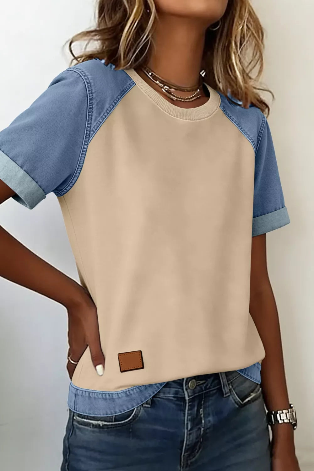 Color block t-shirt with beige front and denim sleeves, round neck, short sleeves, and faux leather patch.