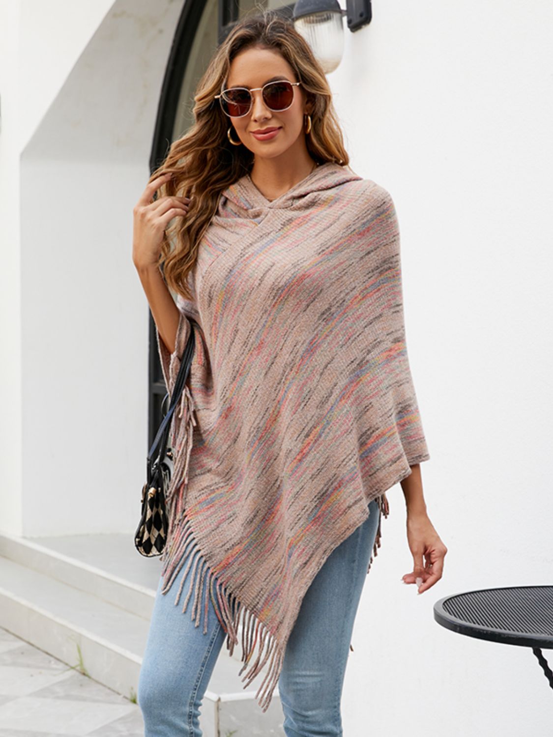 Hooded mélange cape with fringe detail in a neutral multi-color knit, styled casually.