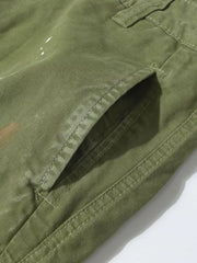 Green distressed cargo pants with white paint accents and visible stitching detail.