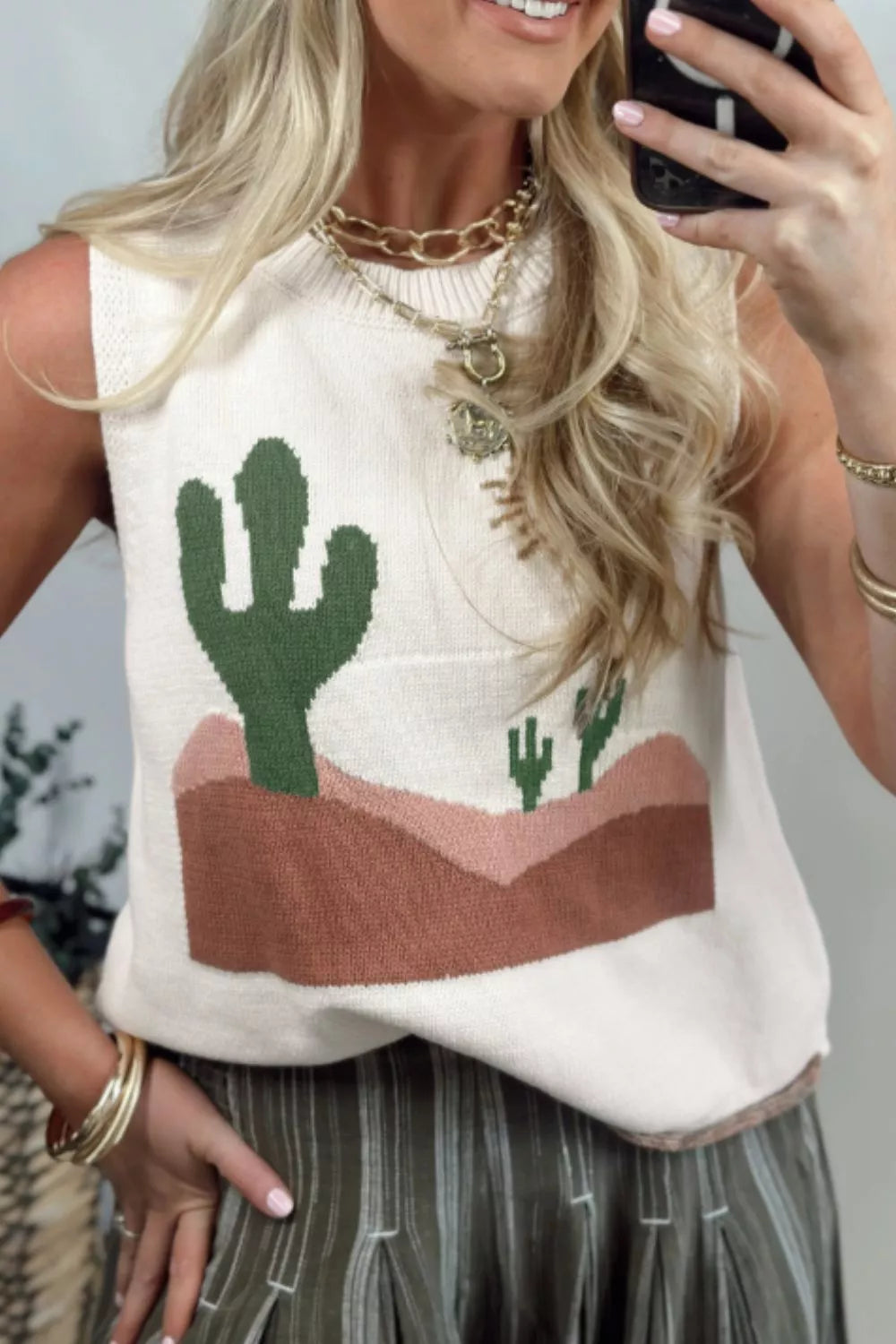 Cream knit sweater vest with a desert cactus graphic, crew neck, sleeveless, and a pocket detail.