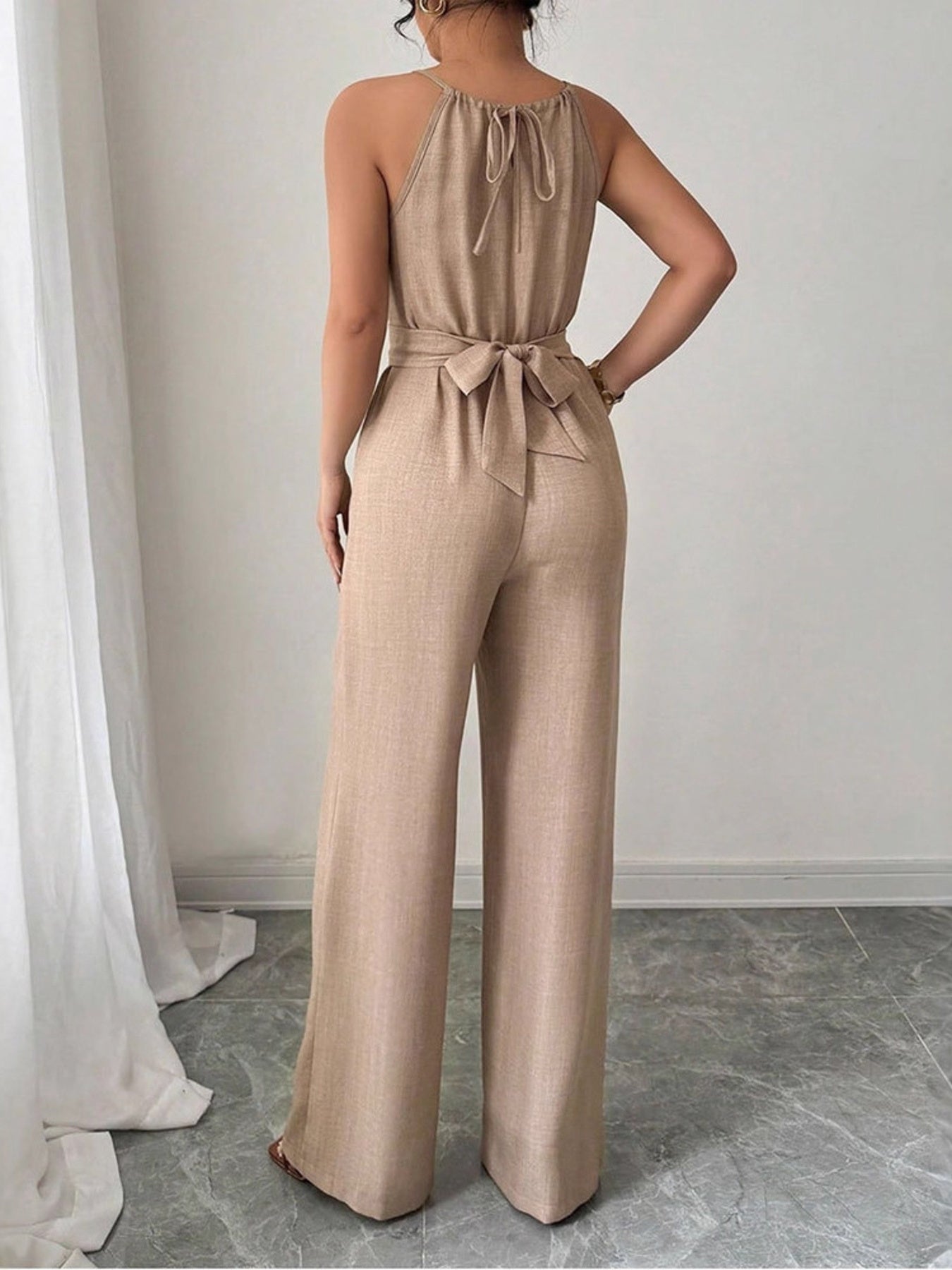 Beige halter neck wide leg jumpsuit with drawstring waist tie and back tie detail.