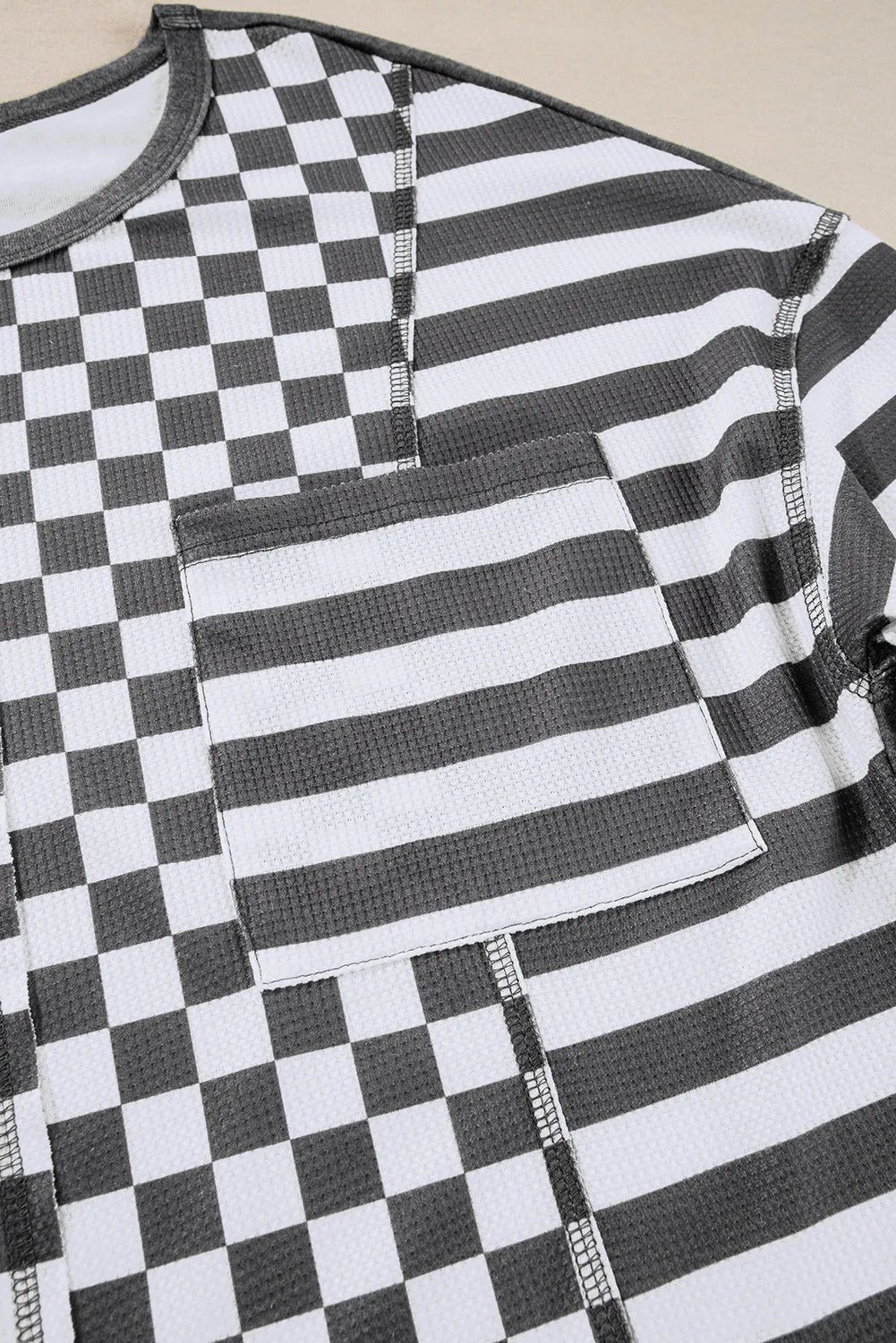 Asymmetrical checkered patchwork knit top with striped pocket in black and white.