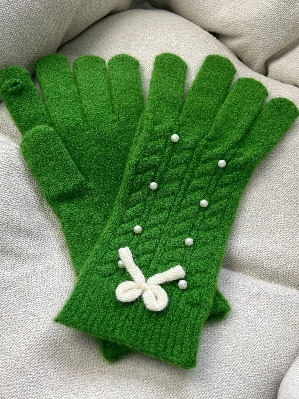 Green cable knit gloves with pearl embellishments and a white bow detail.