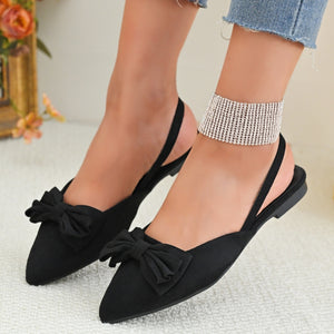 Black slingback flats with pointed toe and bow detail.