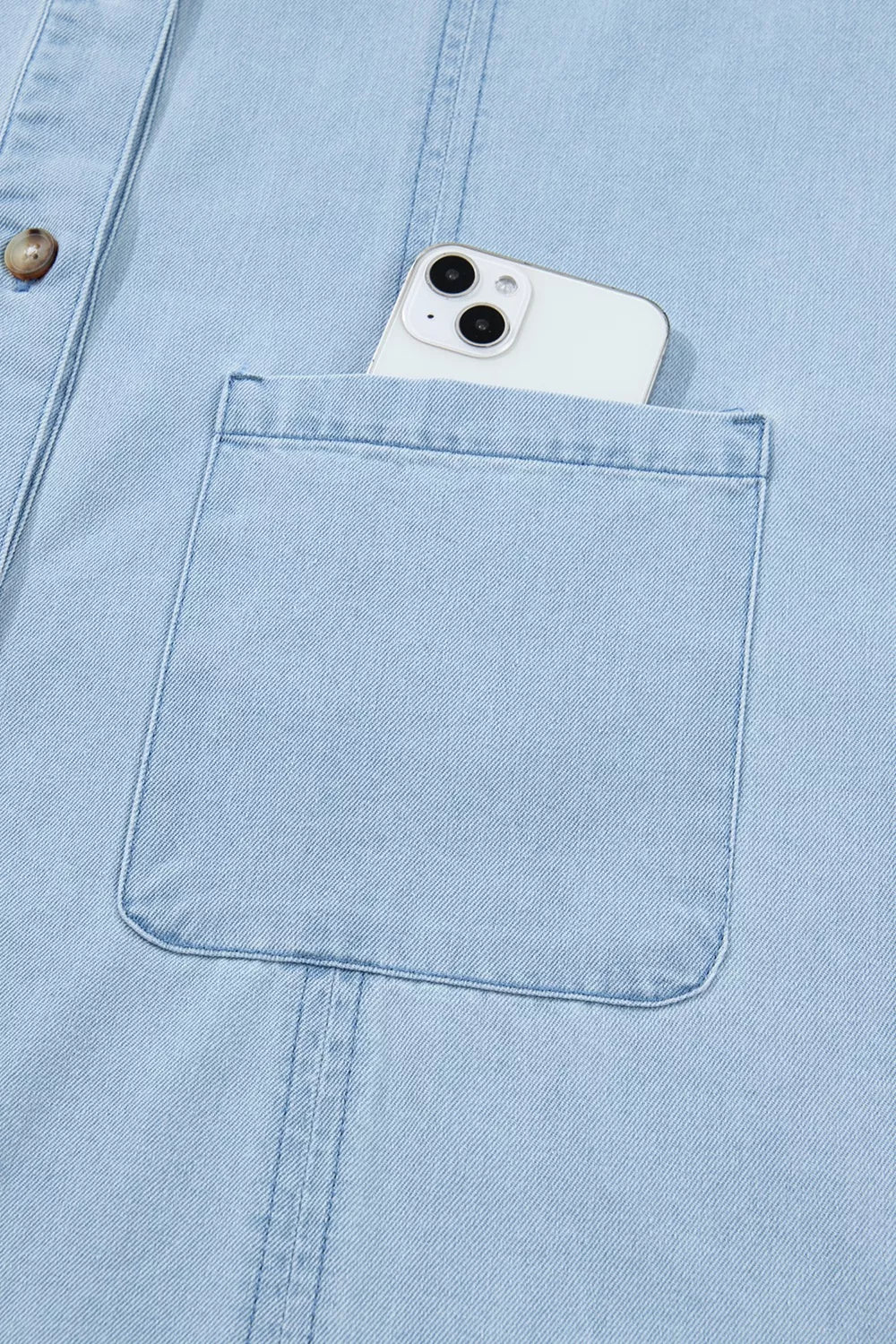 Light blue denim shift dress with button-down front and chest pocket holding a smartphone.