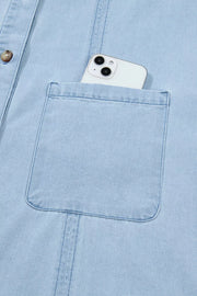 Light blue denim shift dress with button-down front and chest pocket holding a smartphone.