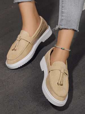 Beige suede loafer slides with tassel detail and white platform sole.