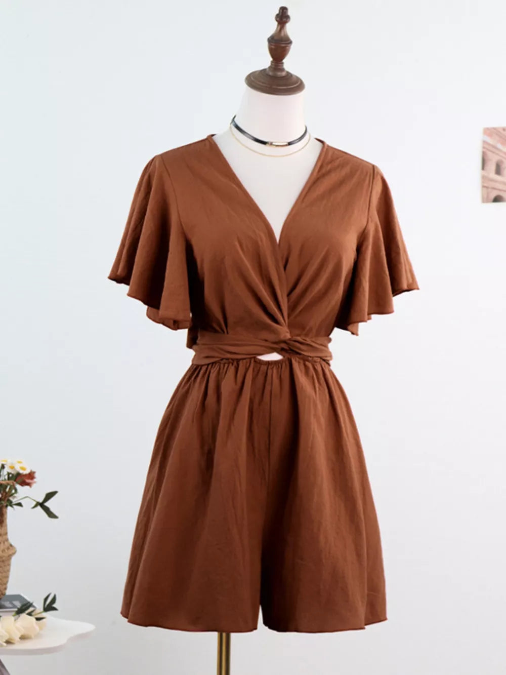 Dark brown cotton romper with flutter sleeves, V-neck, and tie-waist detail.