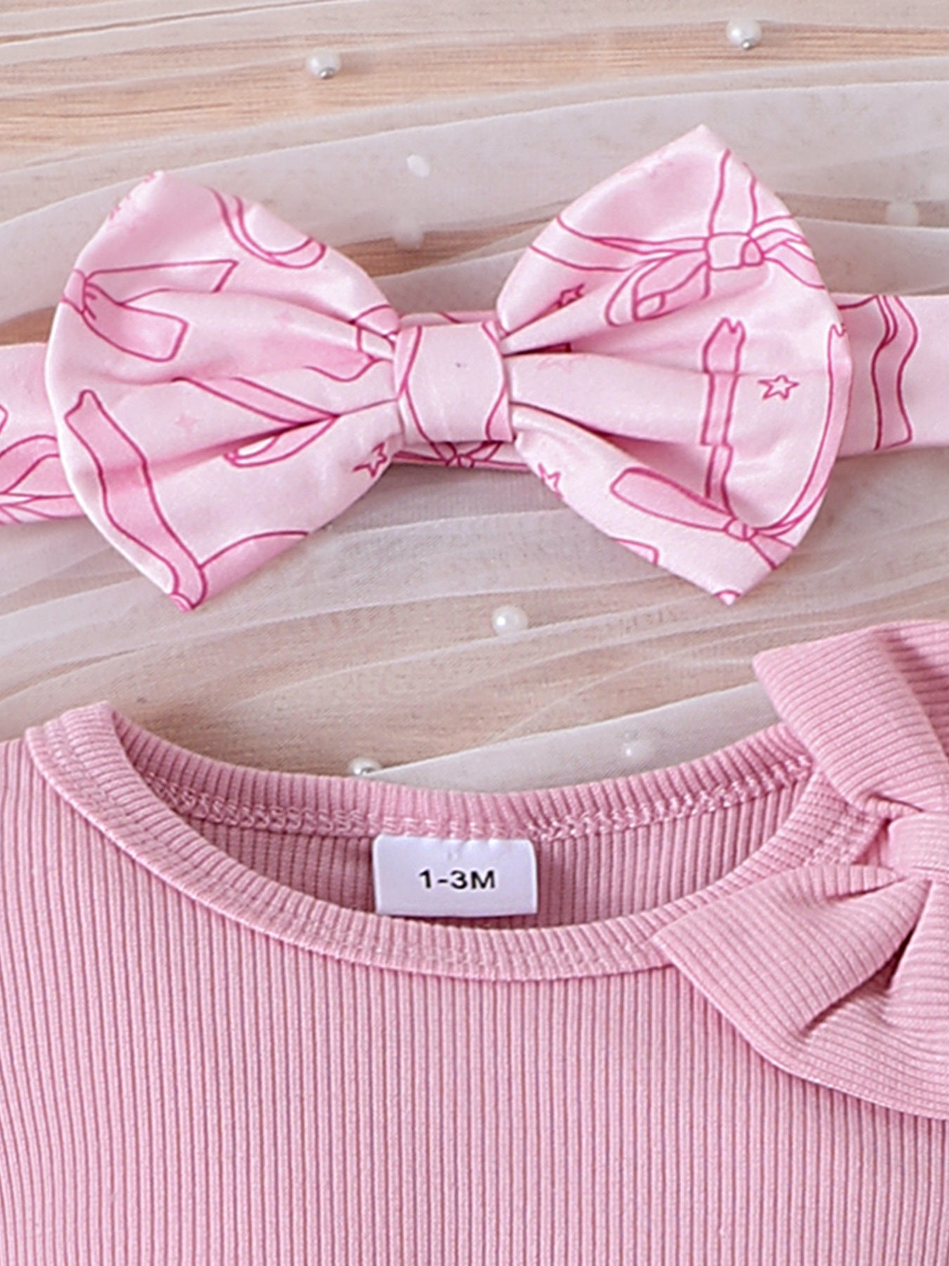 Pink ribbed cotton baby bodysuit with bow detail and matching bowknot headband.